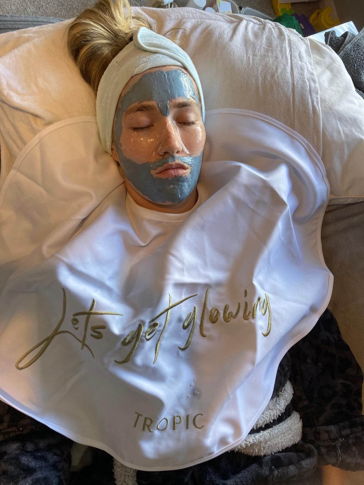 A client relaxing with a Tropic clay mask, wrapped in a 'Let's get glowing' Tropic cape